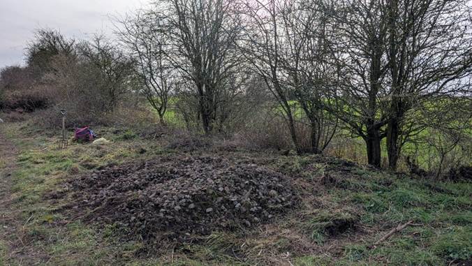 Vegetation has been cleared, showing piles of stones from the railway which used to be at this location