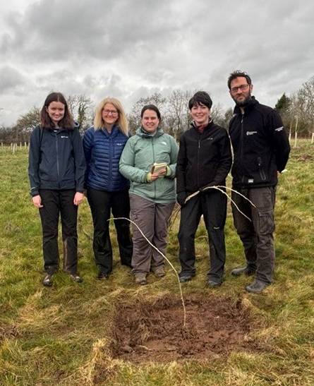 Five people smiling and standing behind a planted Black Poplar at Brackenhurst