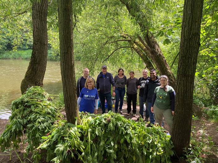 Group of people standing behind a pile of pulled Himalayan Balsam