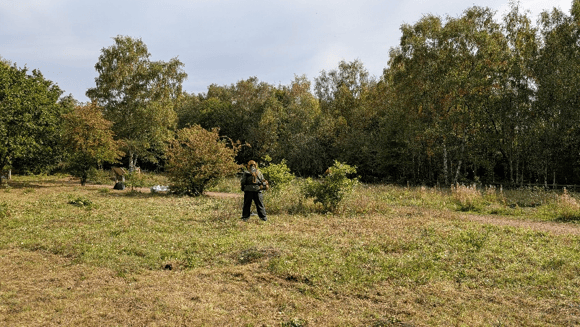 A person in full safety gear brushcutting on a grassland meadow